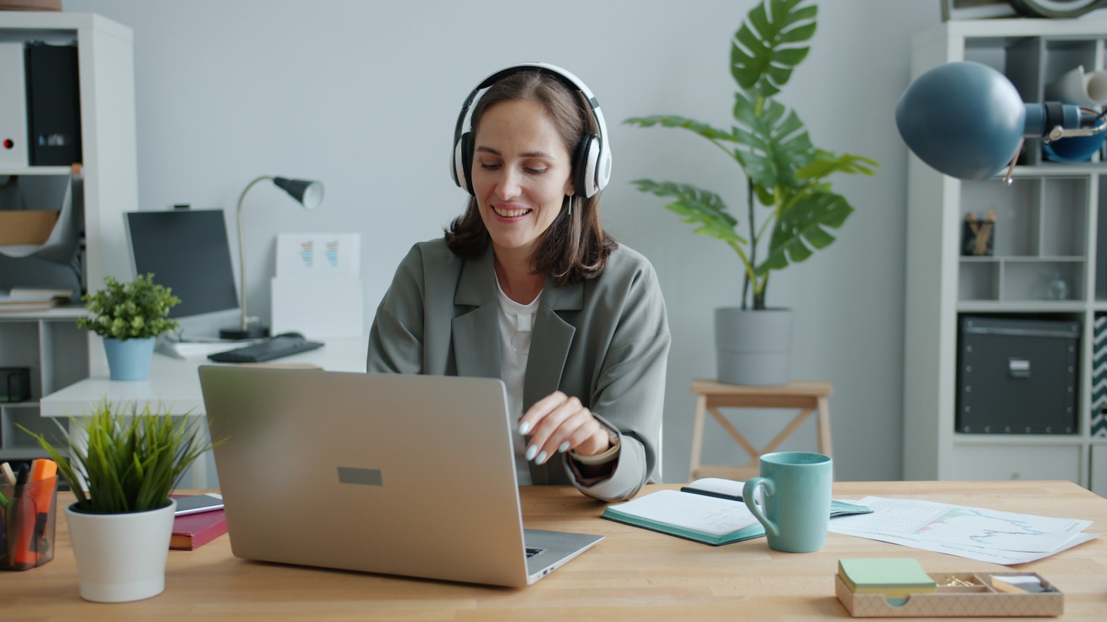 Woman wearing headphones works on a laptop at desk.